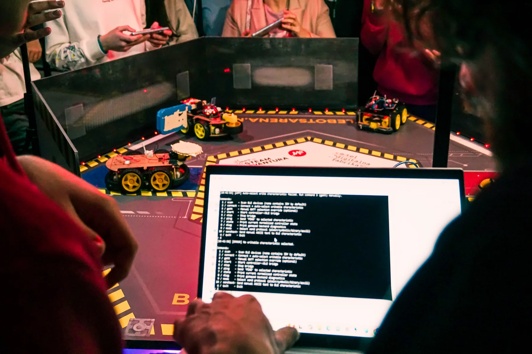 Laptop sa programskim kodom i roboti tokom testiranja u areni